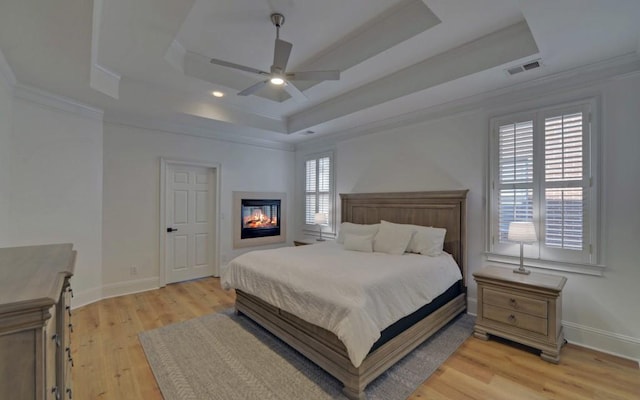 bedroom with ceiling fan, light wood-type flooring, a tray ceiling, and multiple windows