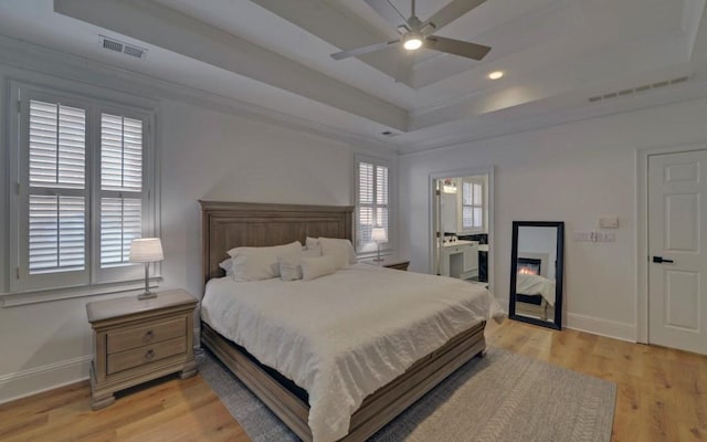 bedroom featuring ceiling fan, connected bathroom, light hardwood / wood-style flooring, and a tray ceiling