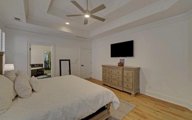 bedroom with ceiling fan, a raised ceiling, ensuite bath, crown molding, and light wood-type flooring