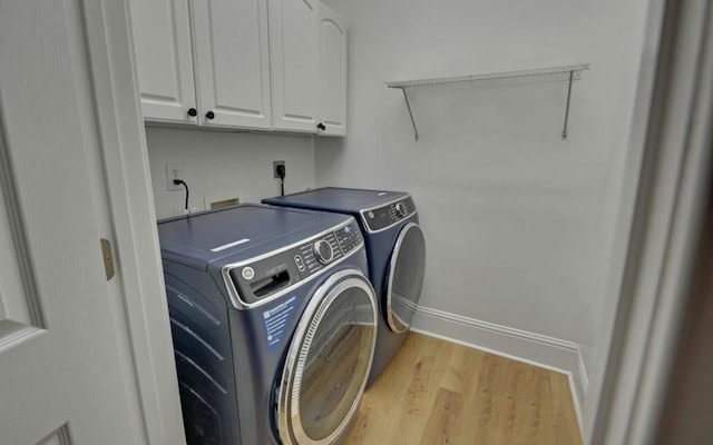 laundry room with light wood-type flooring, washer and dryer, and cabinets