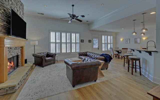 living room with light wood-type flooring, ceiling fan, a stone fireplace, and sink