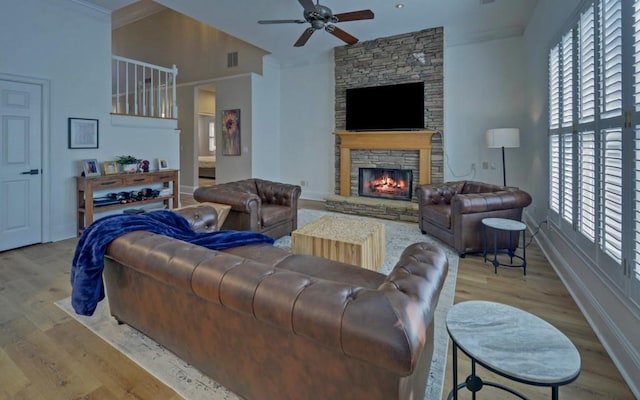 living room featuring ceiling fan, a fireplace, crown molding, and light hardwood / wood-style flooring