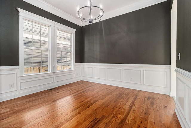 unfurnished dining area with wood finished floors, a wainscoted wall, visible vents, ornamental molding, and a notable chandelier