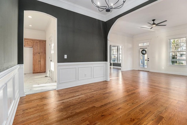 interior space featuring arched walkways, light wood-style floors, ornamental molding, and a decorative wall