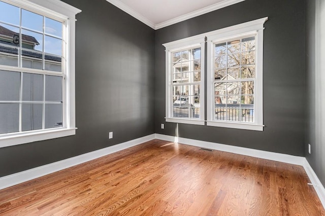 empty room featuring visible vents, wood finished floors, baseboards, and ornamental molding