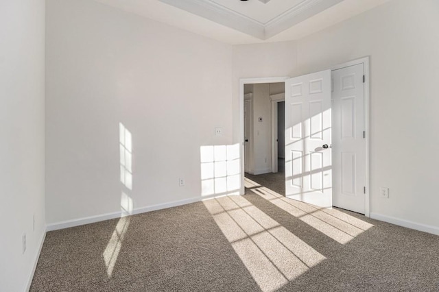 carpeted spare room with baseboards, a raised ceiling, and ornamental molding