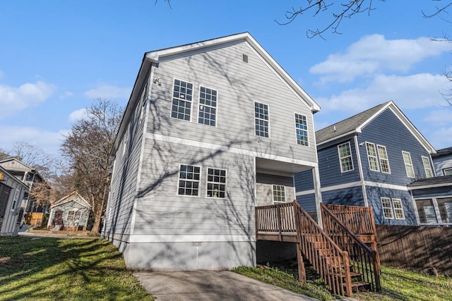 rear view of house featuring a lawn, driveway, a wooden deck, and stairs