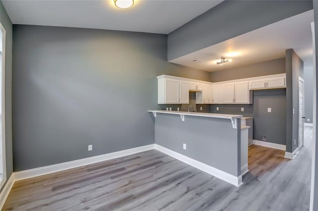 6269 Colonial Vw, Fairburn, GA 30213 - kitchen featuring a peninsula, white cabinets, a kitchen bar, light wood-style floors, and baseboards