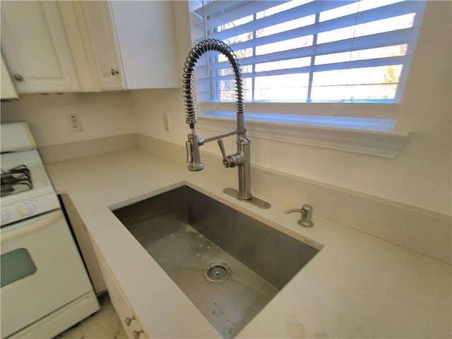 room details with white range with gas stovetop, white cabinets, and sink