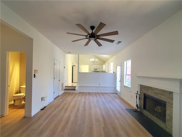 unfurnished living room featuring ceiling fan with notable chandelier, light wood-type flooring, a stone fireplace, and vaulted ceiling