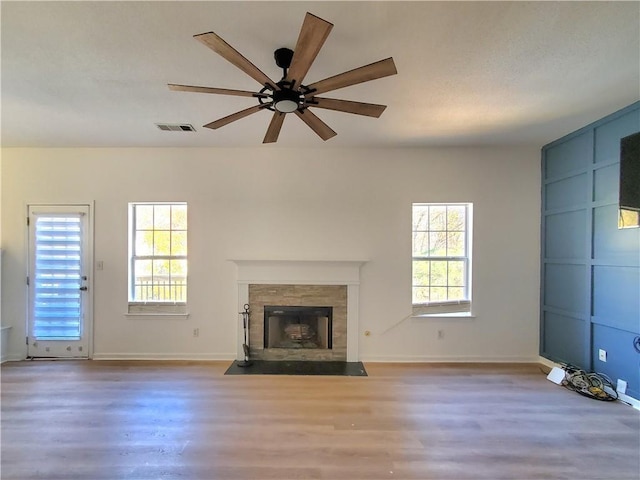 unfurnished living room with hardwood / wood-style floors, ceiling fan, a wealth of natural light, and a tiled fireplace