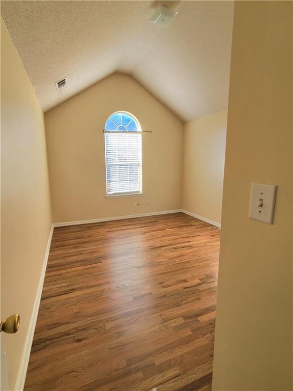 spare room with hardwood / wood-style floors, a textured ceiling, and lofted ceiling