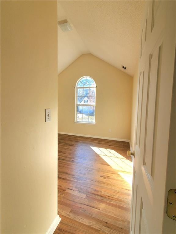 unfurnished room with a textured ceiling, vaulted ceiling, and light hardwood / wood-style flooring