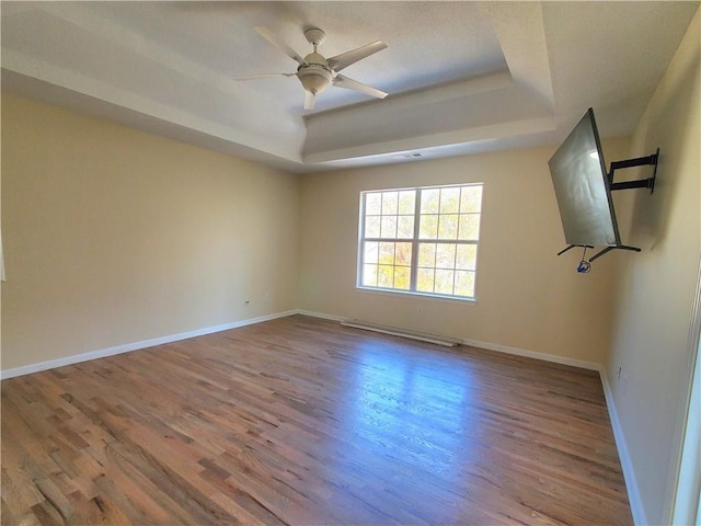 unfurnished room featuring ceiling fan, a baseboard heating unit, wood-type flooring, and a tray ceiling