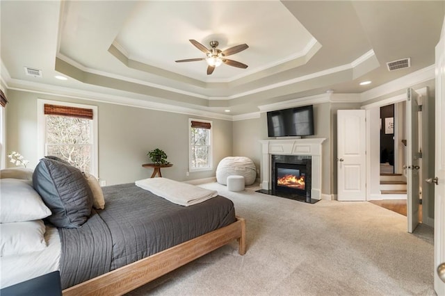 carpeted bedroom with a high end fireplace, visible vents, crown molding, and a tray ceiling