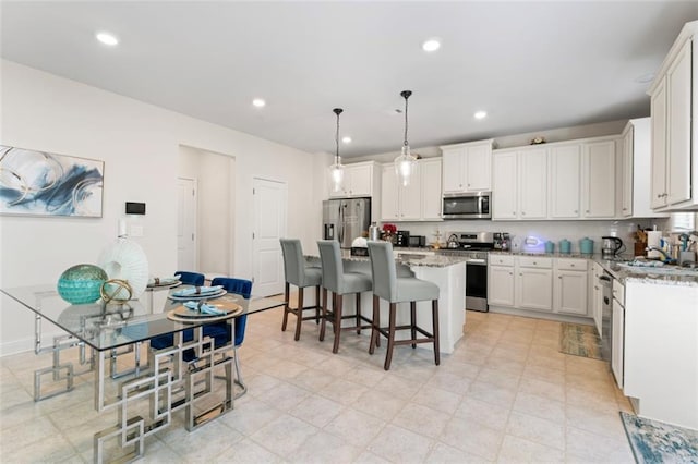 297 Aylesbury Blvd, Mcdonough, GA 30252 - kitchen featuring appliances with stainless steel finishes, a center island, a breakfast bar area, white cabinetry, and decorative light fixtures