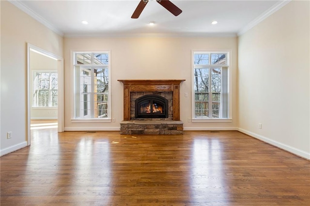 unfurnished living room with crown molding, a stone fireplace, a healthy amount of sunlight, and hardwood / wood-style floors