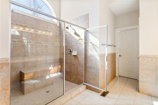 bathroom featuring tile patterned floors, tile walls, tiled shower, and a wainscoted wall