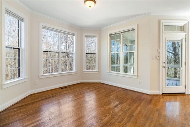 interior space with wood finished floors, baseboards, ornamental molding, and visible vents