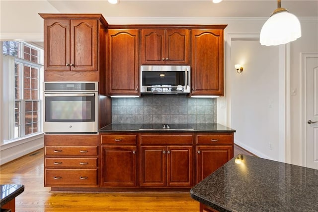 kitchen featuring pendant lighting, backsplash, dark stone counters, ornamental molding, and stainless steel appliances