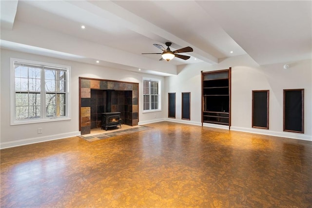 unfurnished living room featuring beam ceiling, a wood stove, a ceiling fan, and baseboards