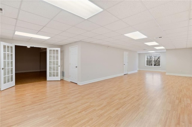 interior space with a paneled ceiling, french doors, and light wood-type flooring