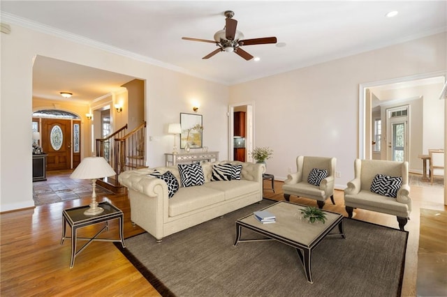 living area with baseboards, a ceiling fan, light wood-style floors, crown molding, and stairs