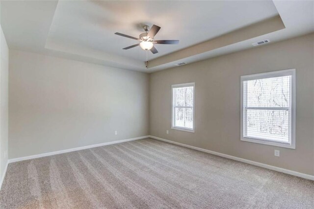 carpeted empty room with ceiling fan and a raised ceiling