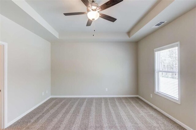 unfurnished room featuring ceiling fan, light colored carpet, and a tray ceiling