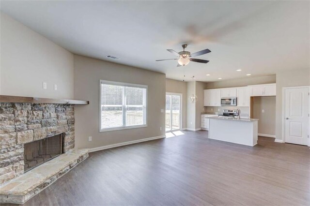 unfurnished living room featuring a stone fireplace, ceiling fan, and dark hardwood / wood-style floors