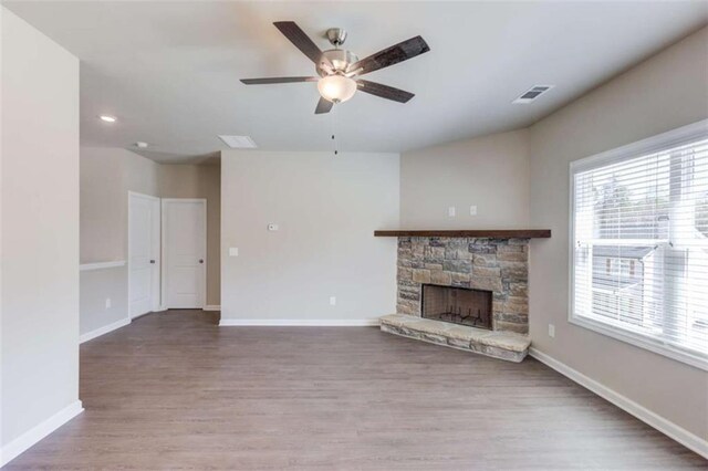 unfurnished living room with ceiling fan, a stone fireplace, and light wood-type flooring