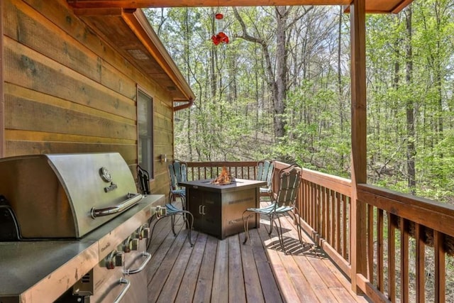 wooden terrace with grilling area, a fire pit, and a view of trees