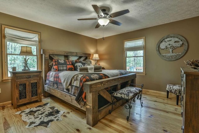 bedroom with a ceiling fan, baseboards, wood-type flooring, and a textured ceiling