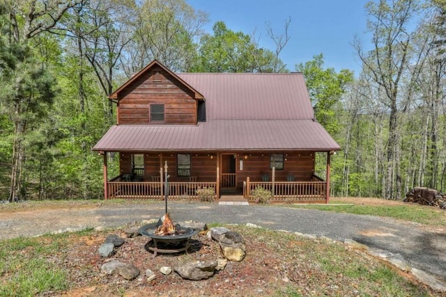 log cabin featuring a porch, a fire pit, gravel driveway, and metal roof