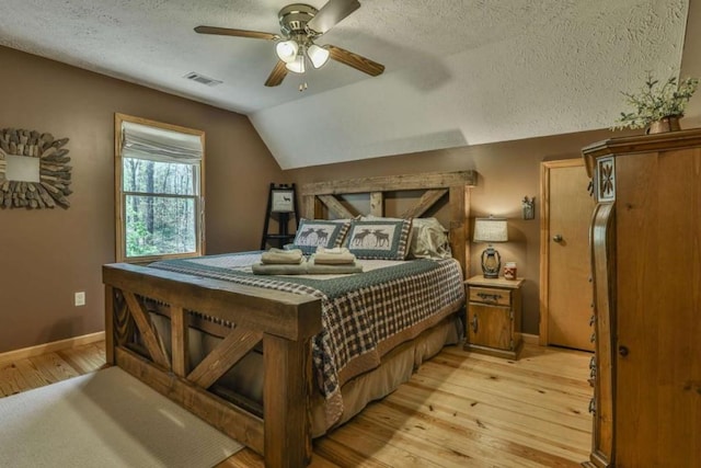 bedroom with visible vents, baseboards, light wood-type flooring, lofted ceiling, and a textured ceiling