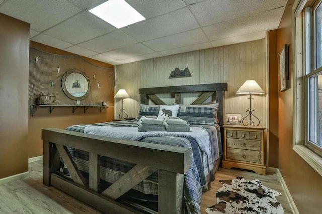 bedroom featuring a drop ceiling, baseboards, and wood finished floors