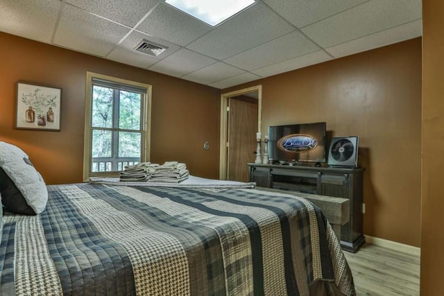 bedroom featuring light wood finished floors, visible vents, baseboards, and a drop ceiling