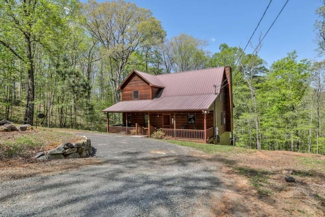 view of front of property featuring a forest view, metal roof, gravel driveway, and covered porch