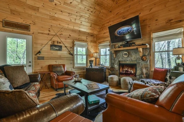 living room with wooden walls, high vaulted ceiling, a stone fireplace, and wood finished floors