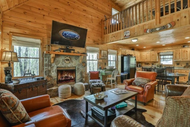 living area with wooden walls, wood ceiling, light wood-type flooring, a fireplace, and high vaulted ceiling