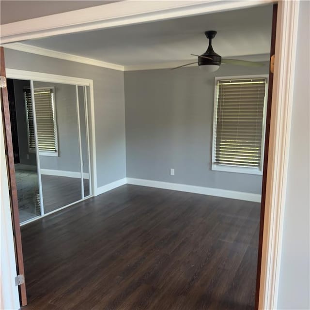 empty room featuring crown molding, baseboards, ceiling fan, and dark wood-type flooring