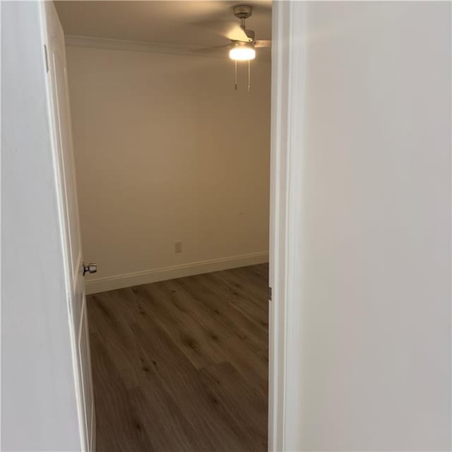 empty room featuring crown molding, dark wood-style flooring, a ceiling fan, and baseboards