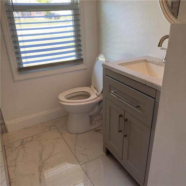 bathroom with toilet, marble finish floor, vanity, and baseboards