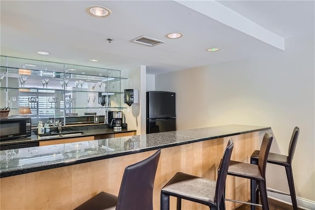 bar with sink, black appliances, and dark stone counters