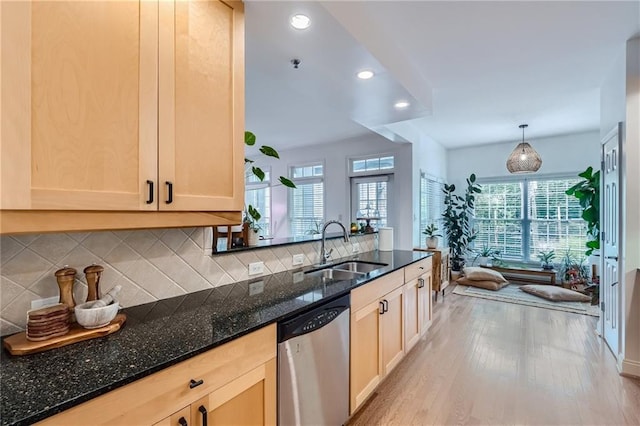 kitchen with dark stone countertops, sink, stainless steel dishwasher, light brown cabinets, and hanging light fixtures