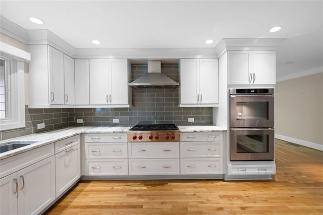 465 Willowbrook Dr SE, Smyrna, GA 30082 - kitchen featuring stainless steel appliances, wall chimney exhaust hood, white cabinets, light wood-style flooring, and tasteful backsplash