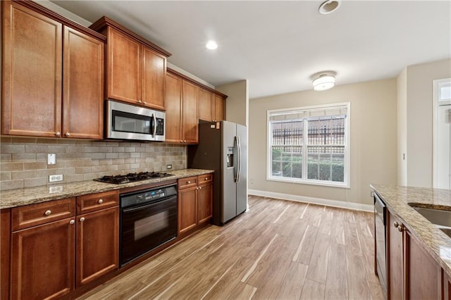 kitchen featuring decorative backsplash, light stone countertops, stainless steel appliances, and light hardwood / wood-style flooring