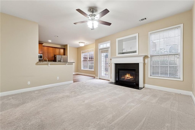 unfurnished living room with light carpet, plenty of natural light, and ceiling fan