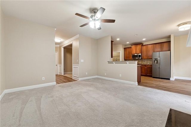 unfurnished living room featuring light colored carpet, ceiling fan, and ornamental molding