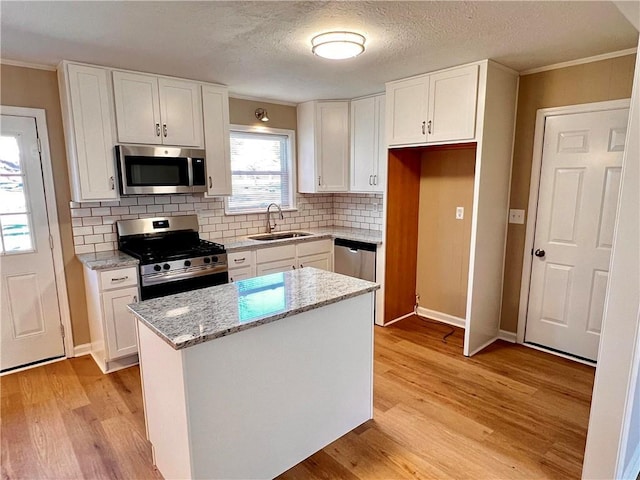 kitchen with white cabinetry, sink, a center island, light stone counters, and appliances with stainless steel finishes